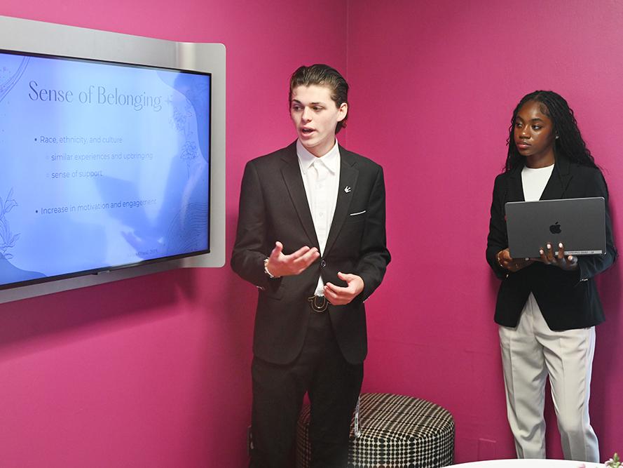 A student stands next to a monitor while giving a presentation.