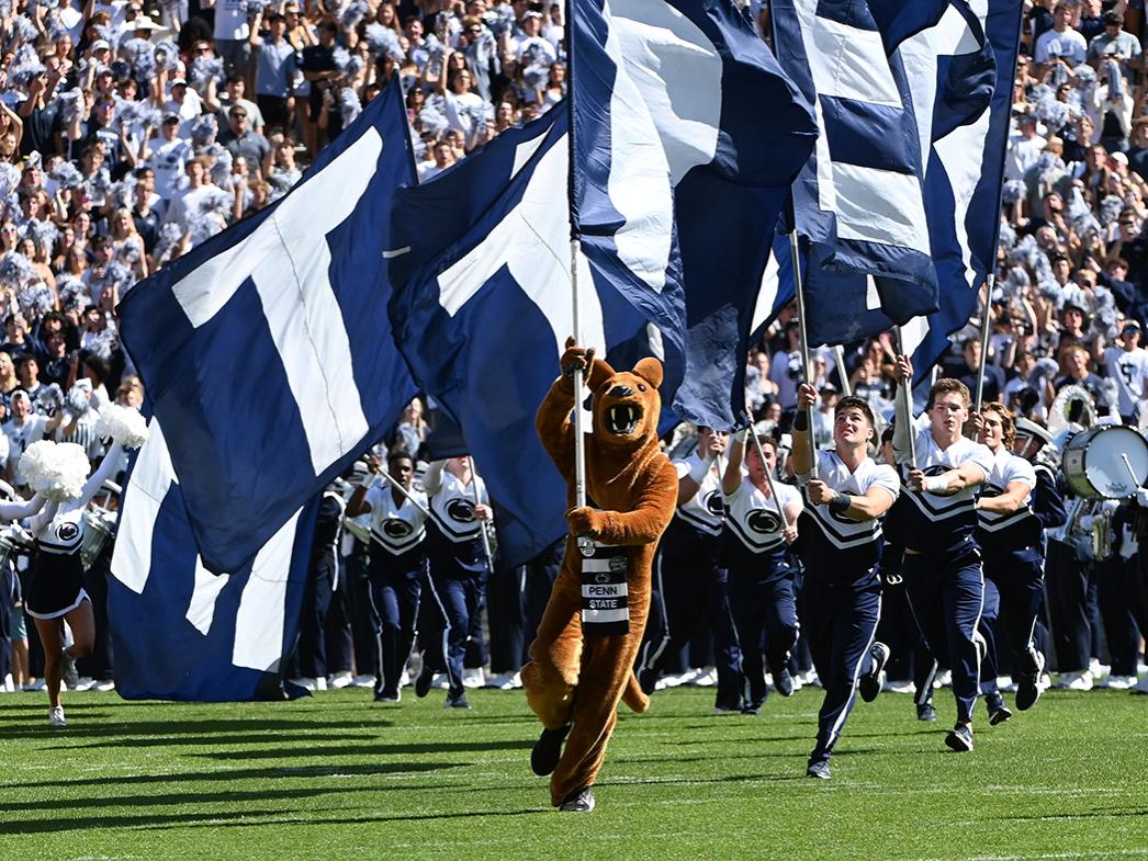 Nittany Lion runs with flags on field