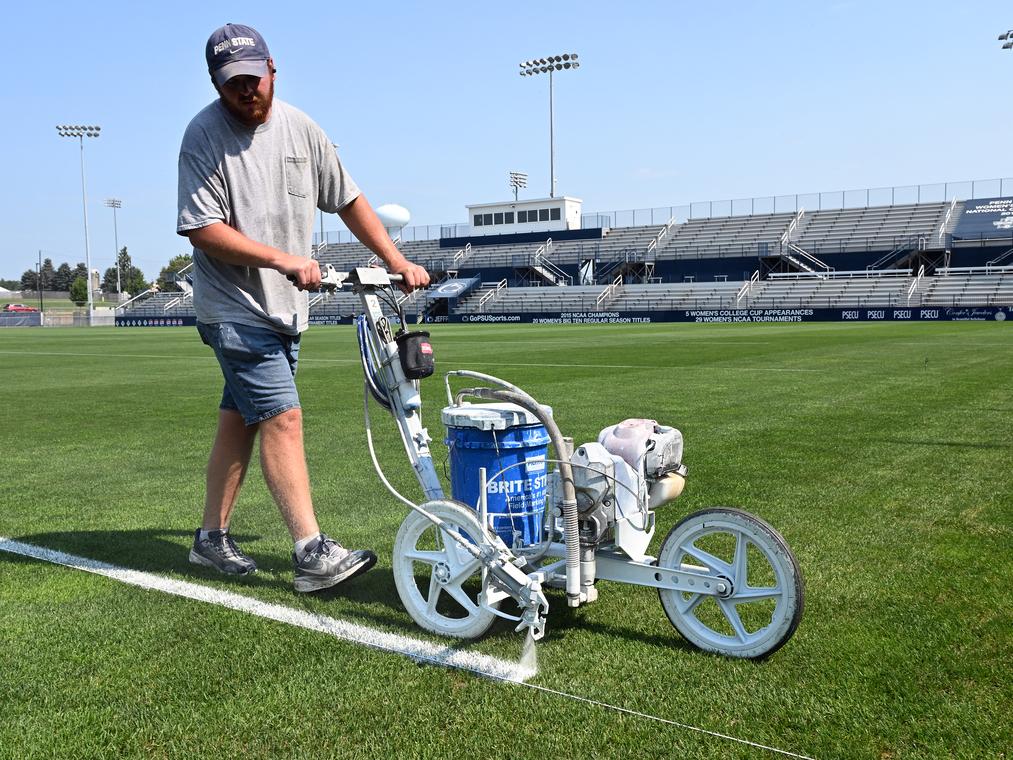 A staff member uses a tool to paint lines on an athletic field