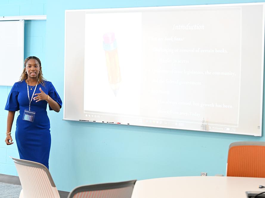 A student stands next to a projector screen while giving a presentation.