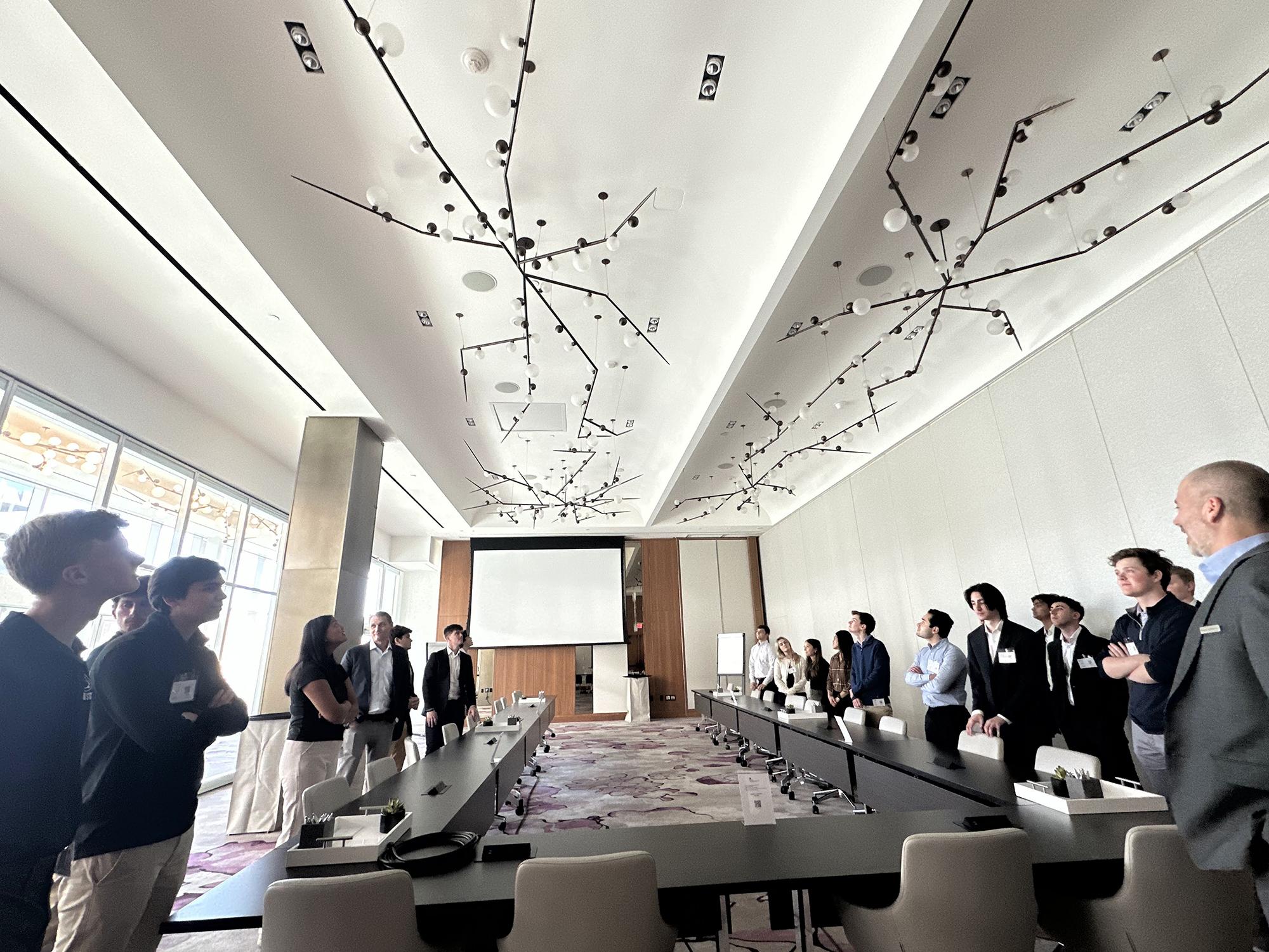 A group of students in business attire gather around a board room table in a hotel