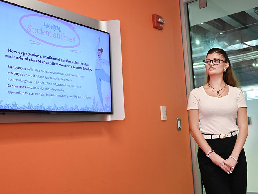 A student stands next to a monitor while giving a presentation.
