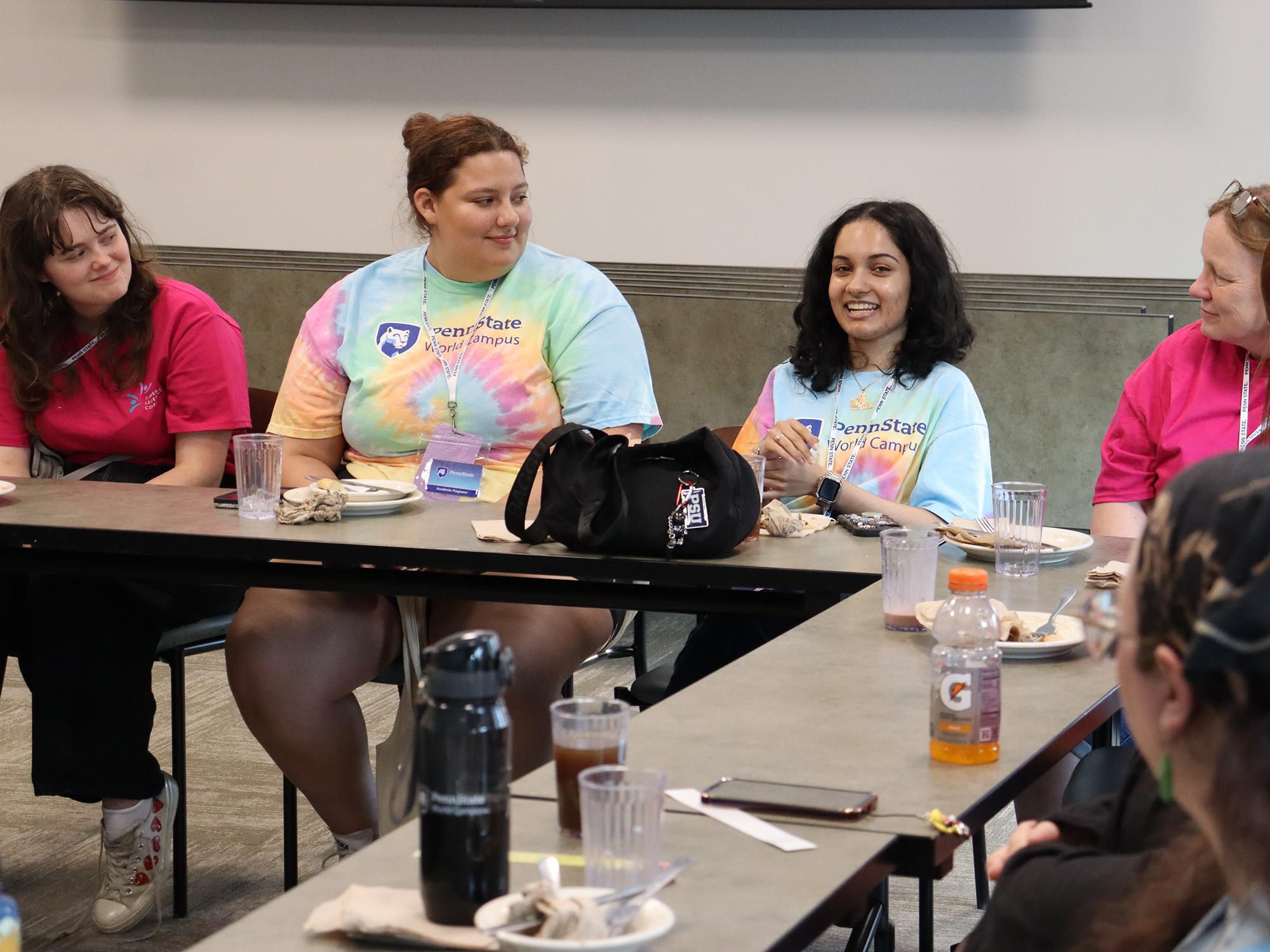 People wearing tie-dye and pink T-shirts listen to a person speak.