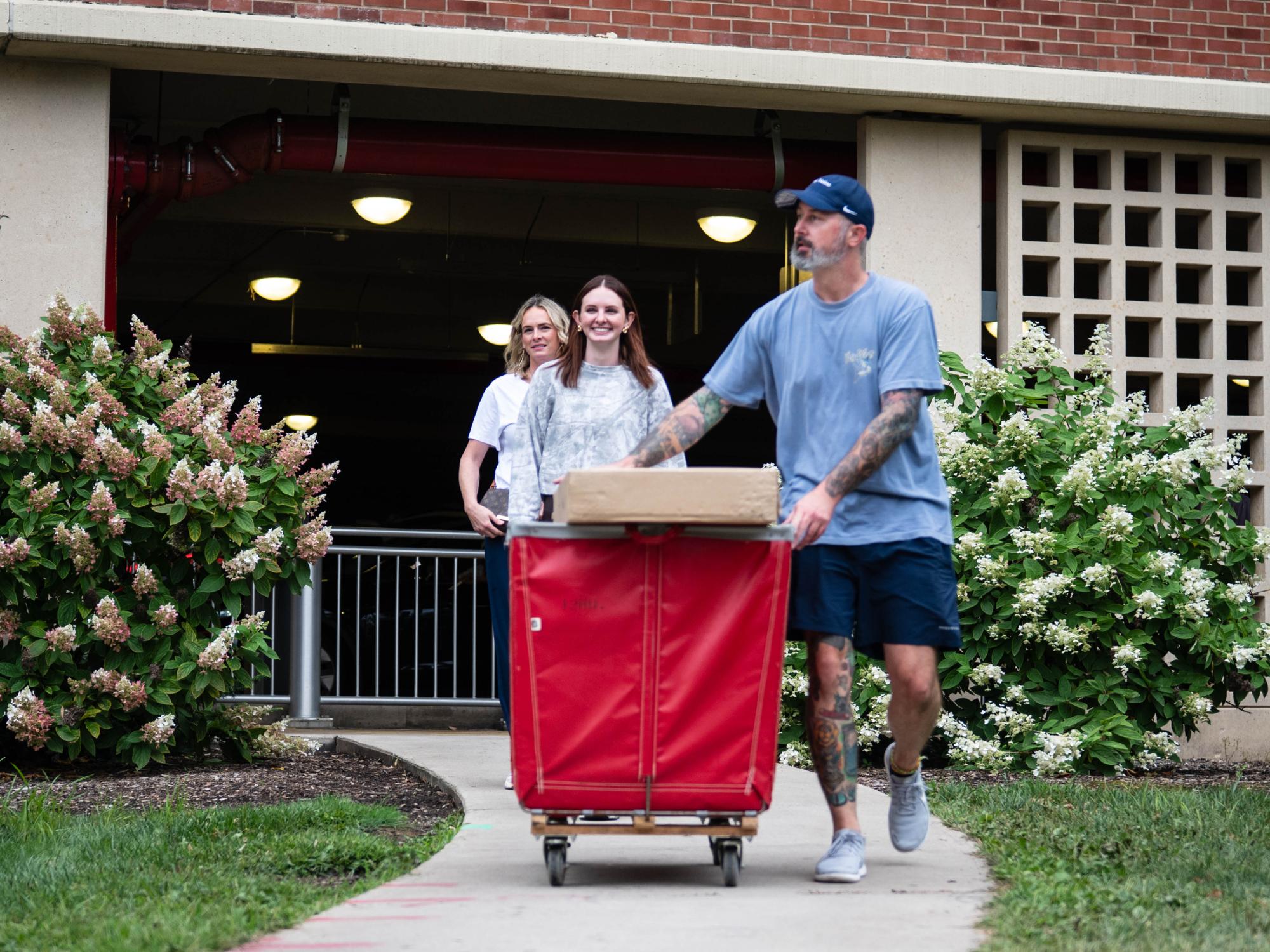 A student's family assists with pushing a red bin on wheels 