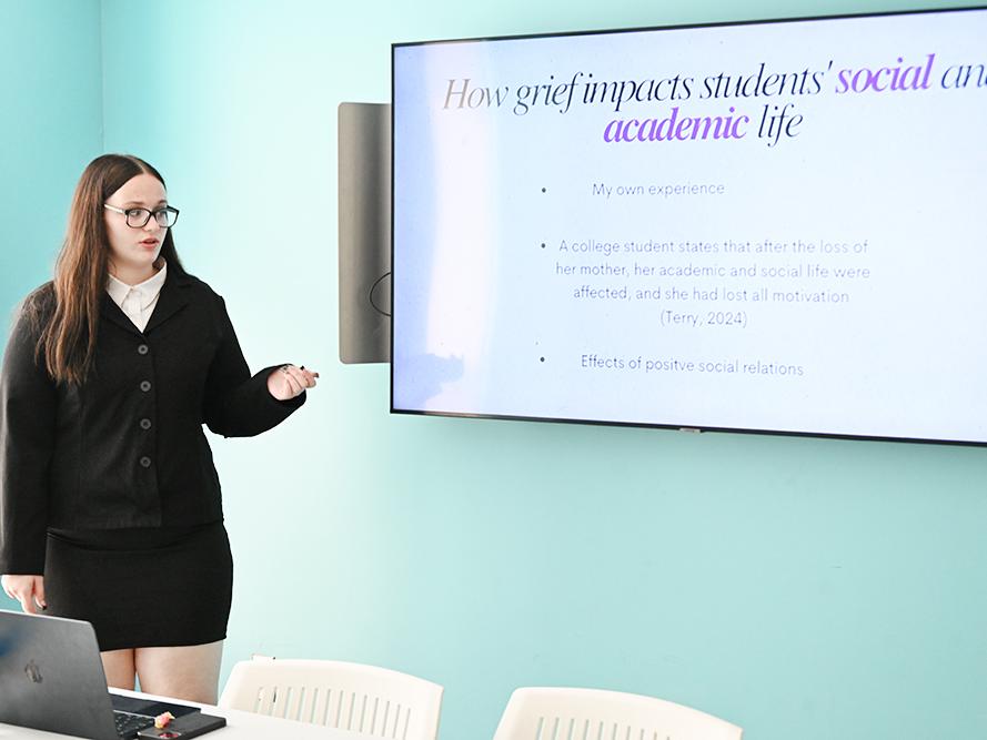 A student stands next to a monitor while giving a presentation.