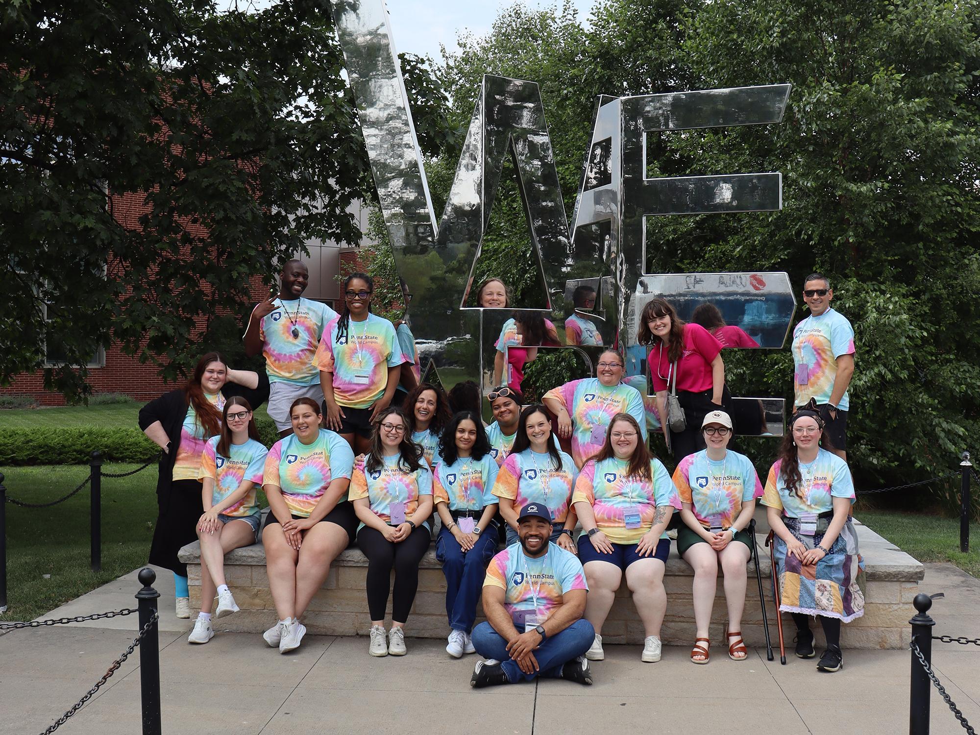 A group of people posing around a metallic, mirror statue.
