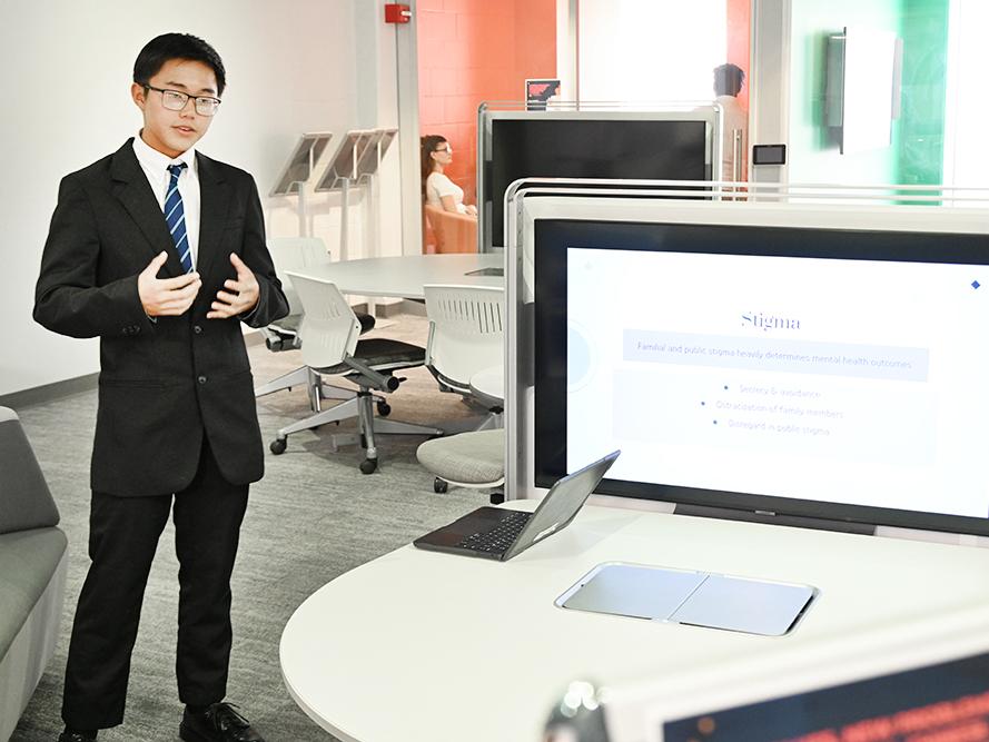 A student stands next to a monitor while giving a presentation.