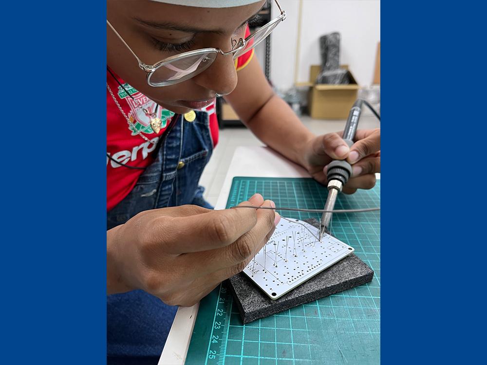 Student sitting close to a Arduino, soldering metal to it.
