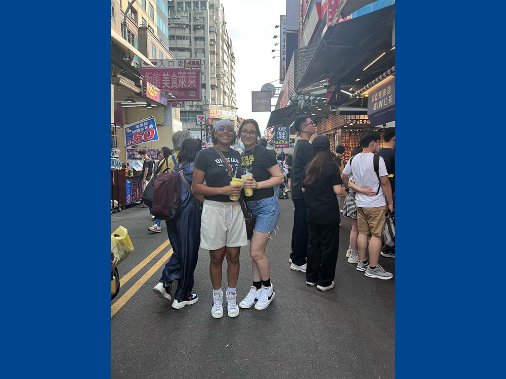 Two students in a busy city center surrounded by people and shops.