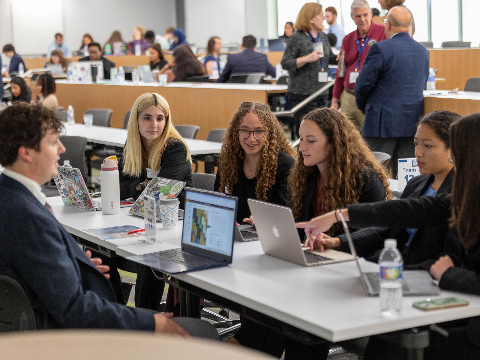 Six students with laptops collaborate during the policy simulation