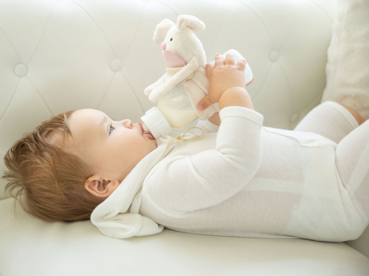 A baby laying down drinking from a bottle with one of the Bottimals products attached to the bottle