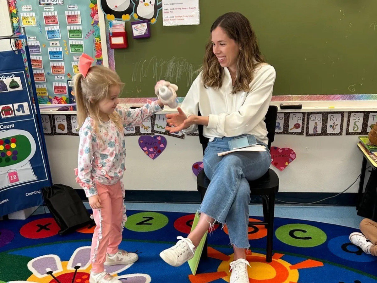 Julianne sits in front of classroom holding the Bottimals product, a child standing next to her looking at the product.