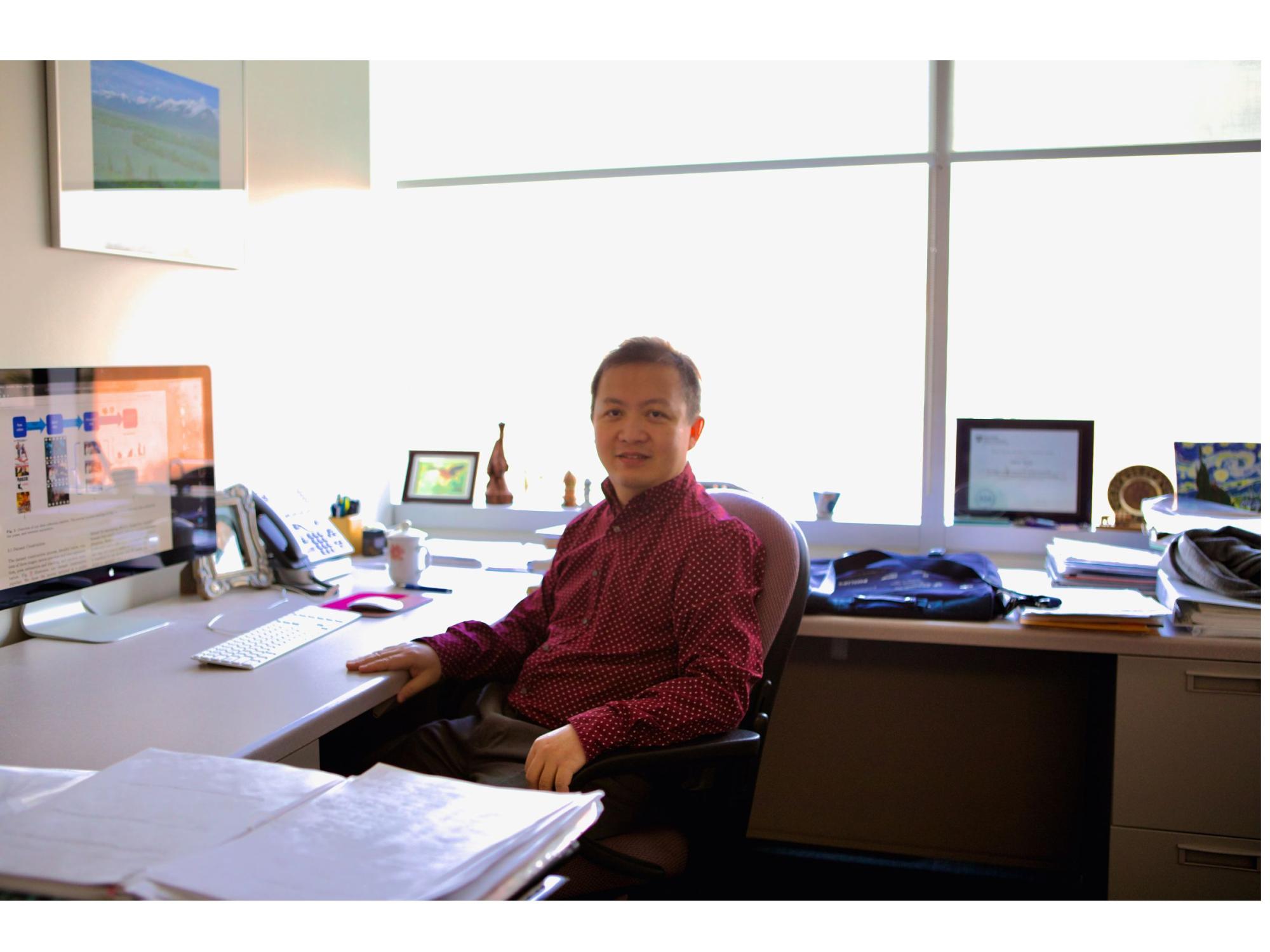 dark-haired person in red shirt seated at office desk