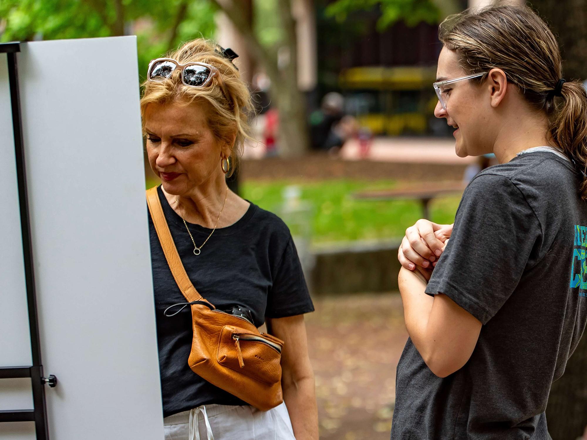 Two people looking at art propped up on an easel in a park.