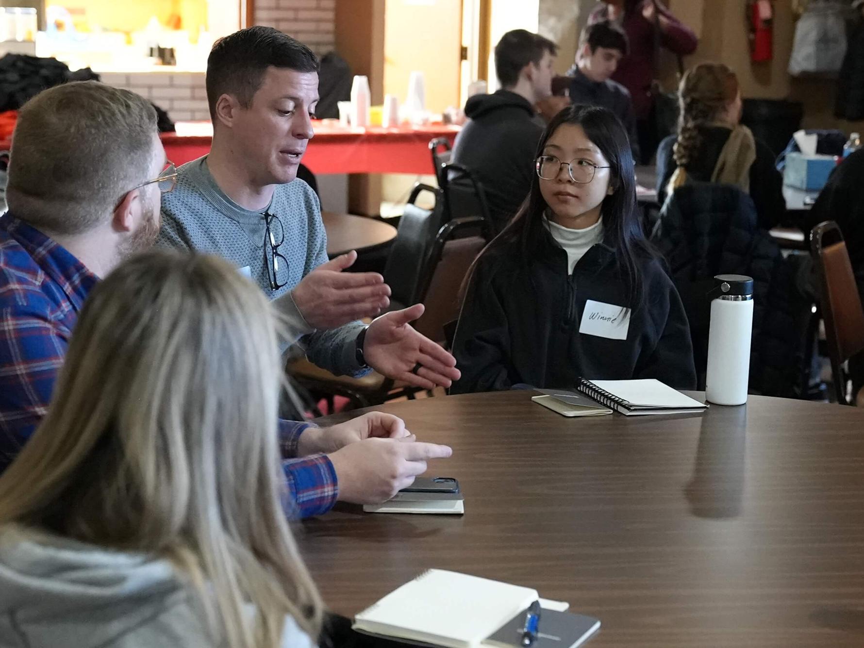 Adults sitting at a round table having a discussion.