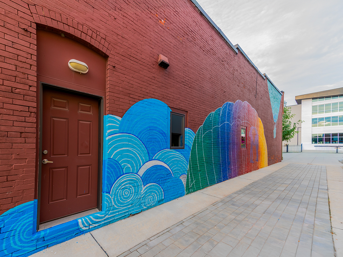 A colorful mural of swirling clouds painted along a brick wall in Buxton Alley, leading toward the town square.