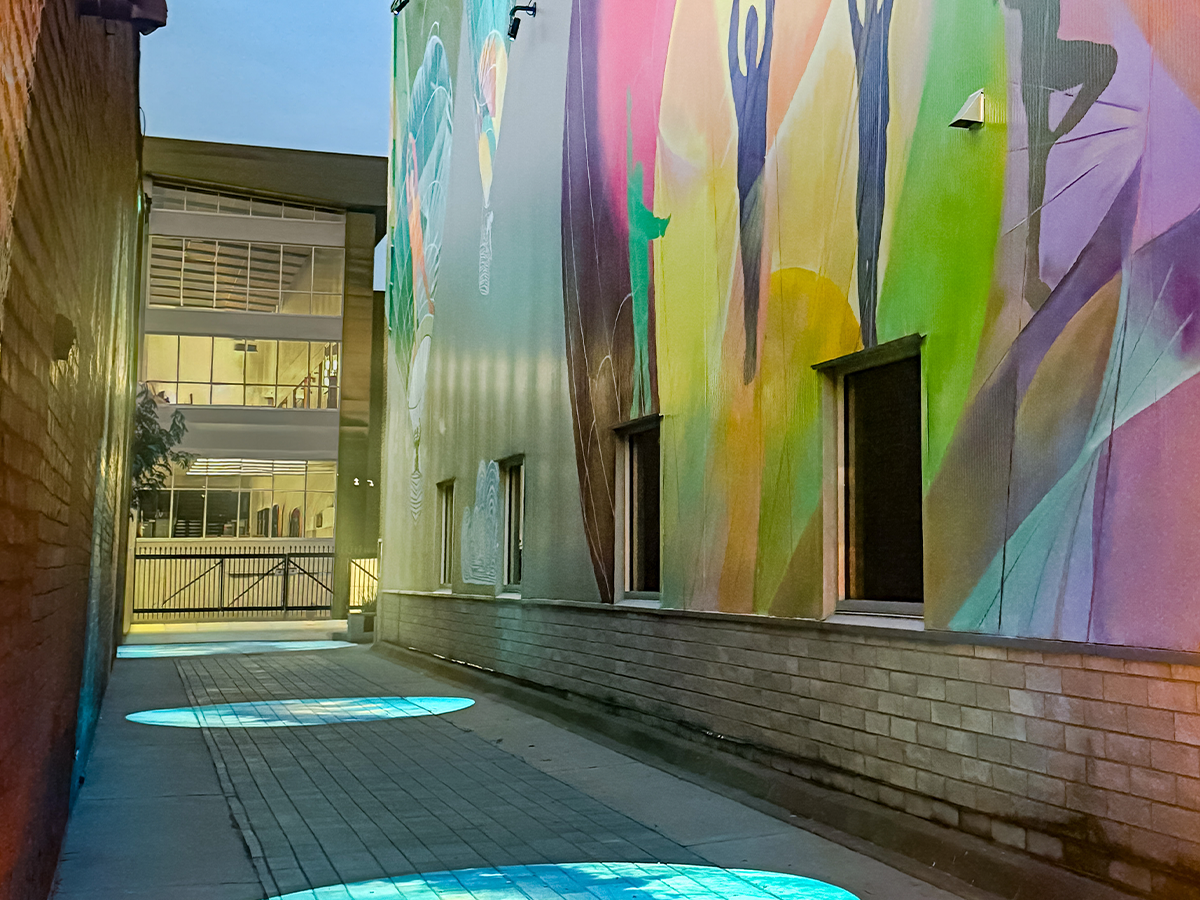 The Buxton Alley mural at night, illuminated by projected light effects on the walkway and colorful designs along the walls.