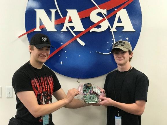 Two men holding an experiment in front of a NASA sign