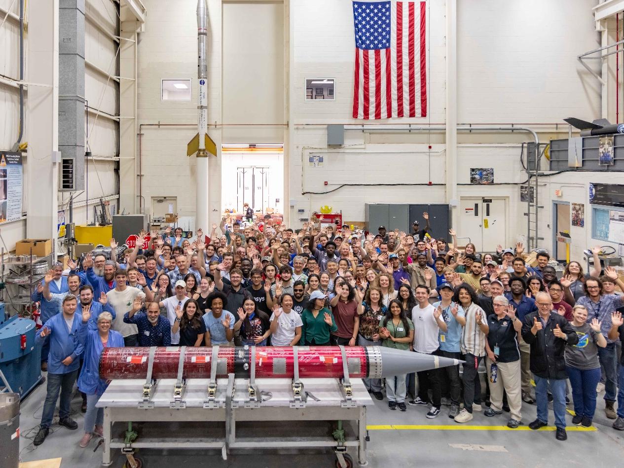 Large group of people standing behind a rocket