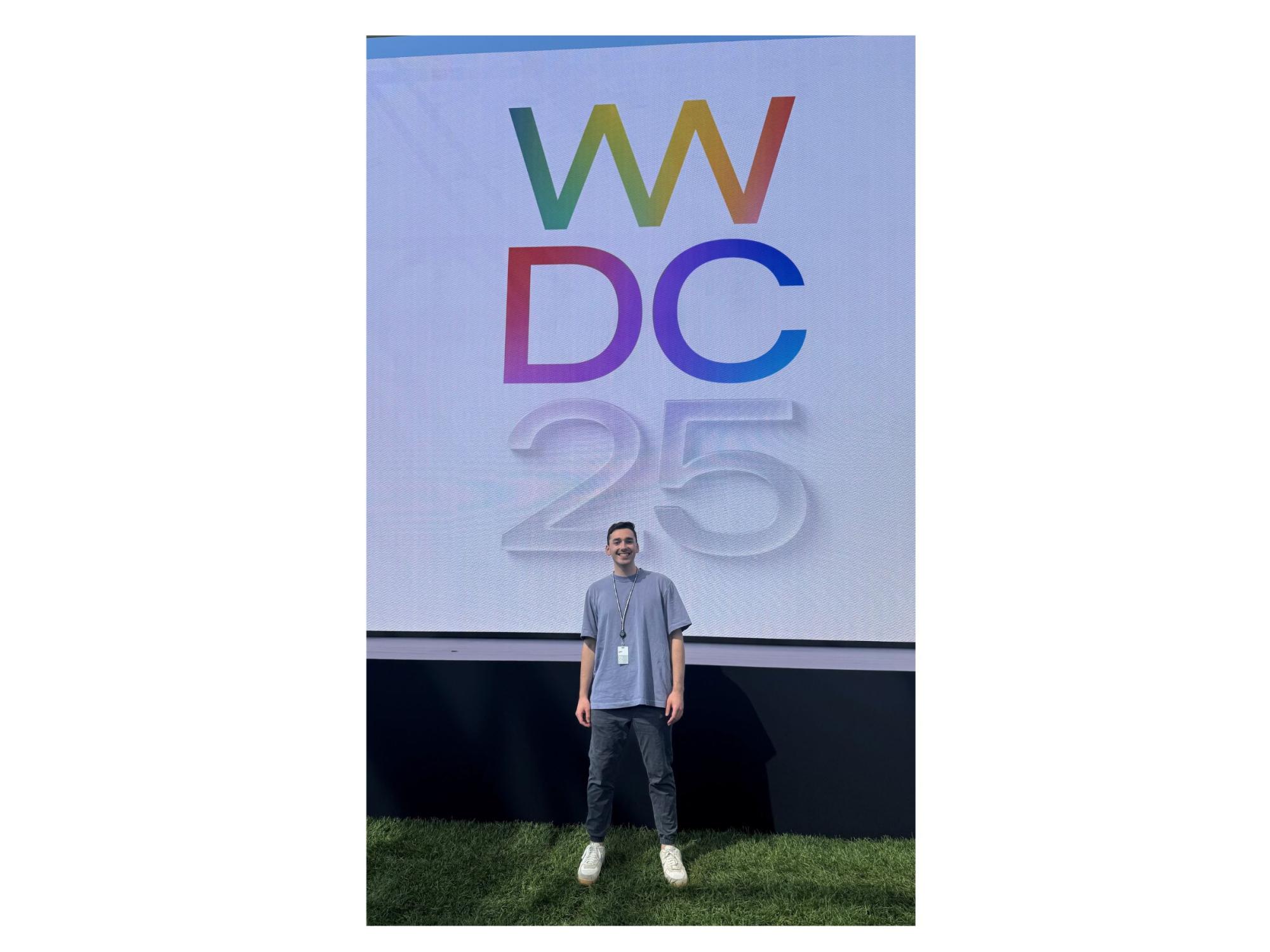 dark-haired person with lanyard stands in front of large WWDC25 sign