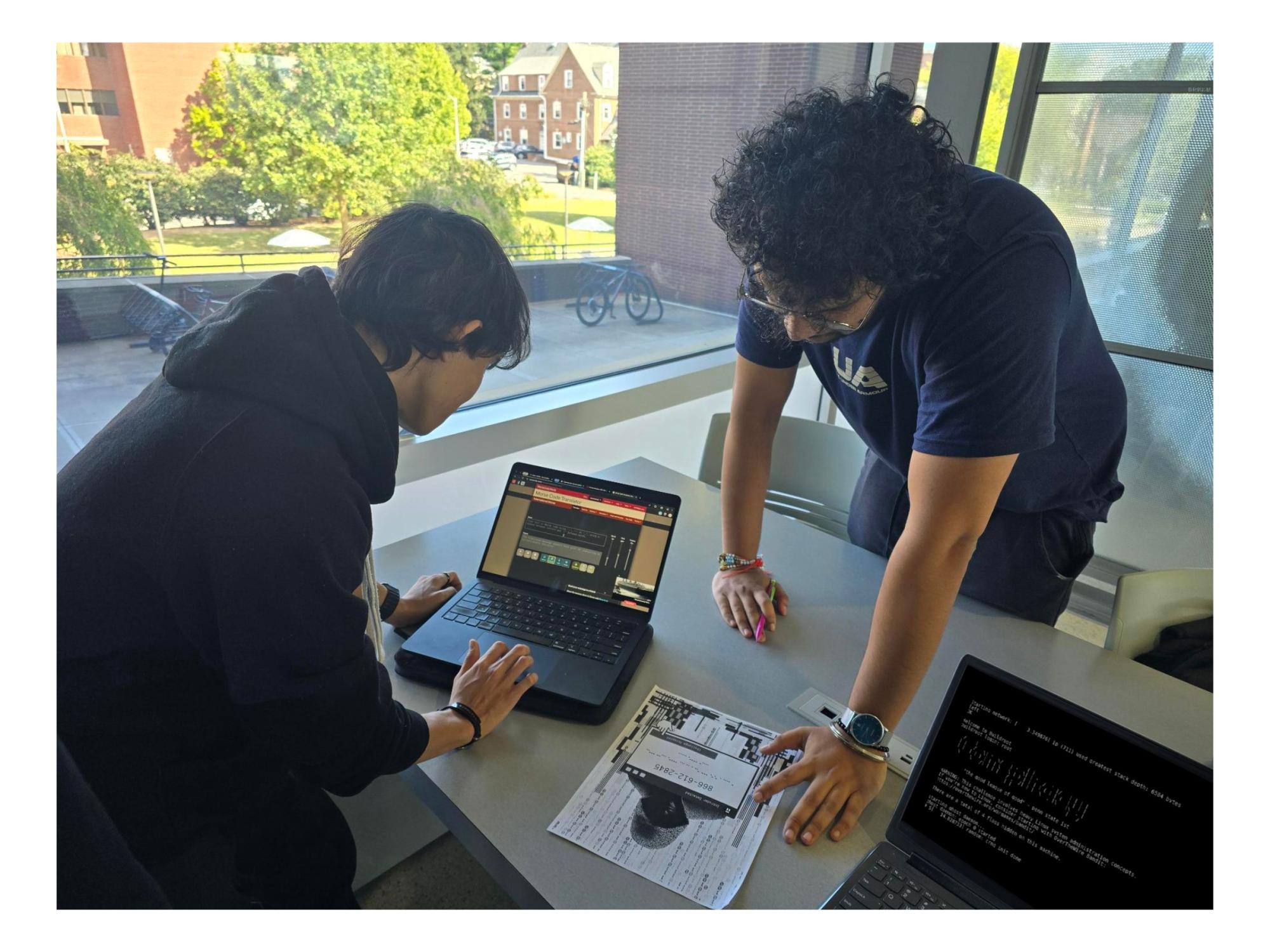 two college students standing at table and looking at laptop