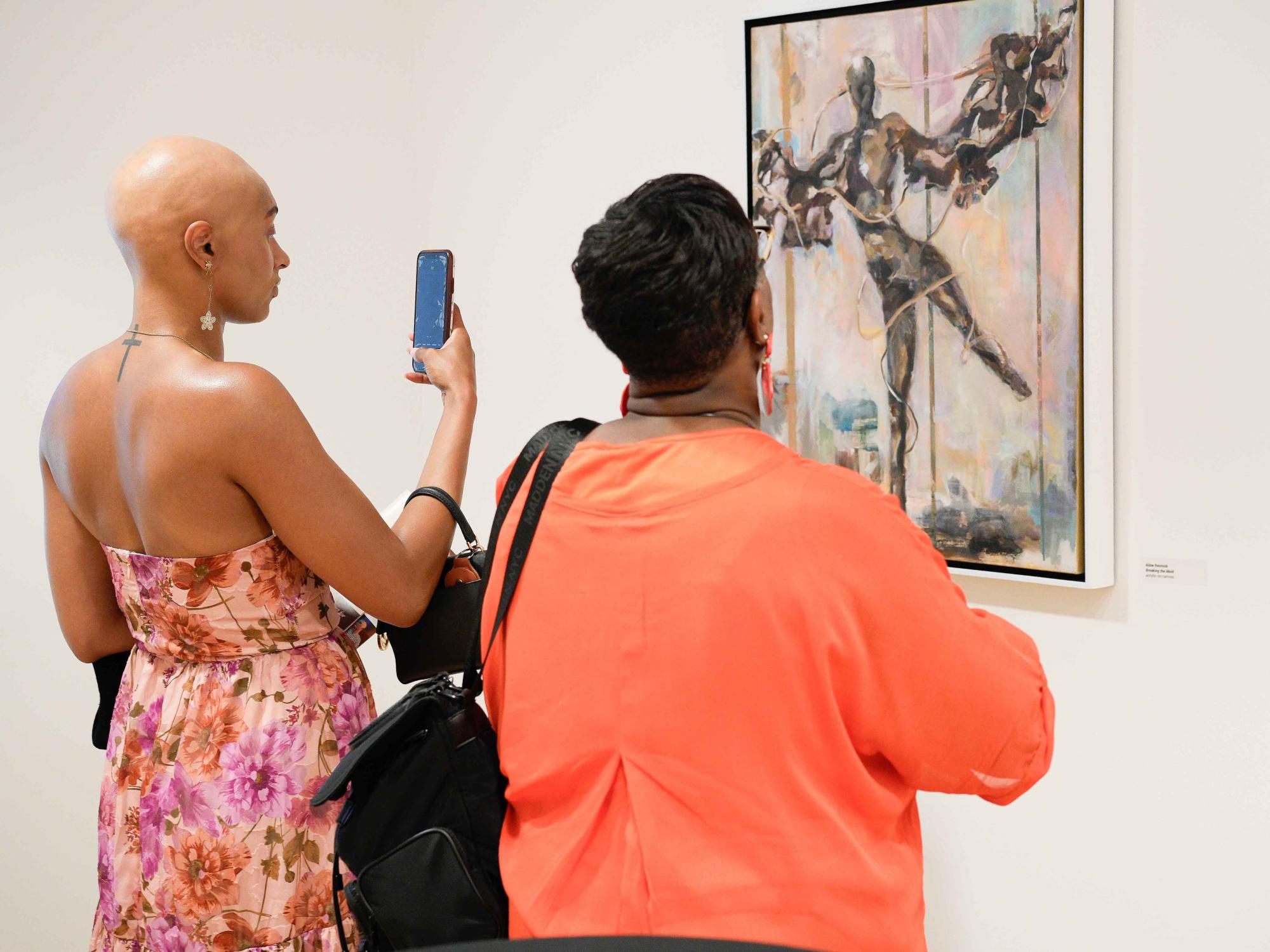Two women look at a painting on a gallery wall