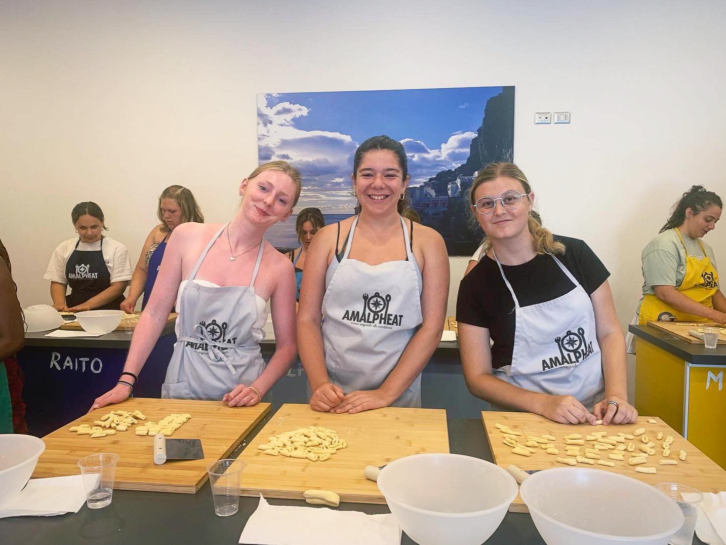 Three Penn State students smile while wearing aprons and making pasta. 