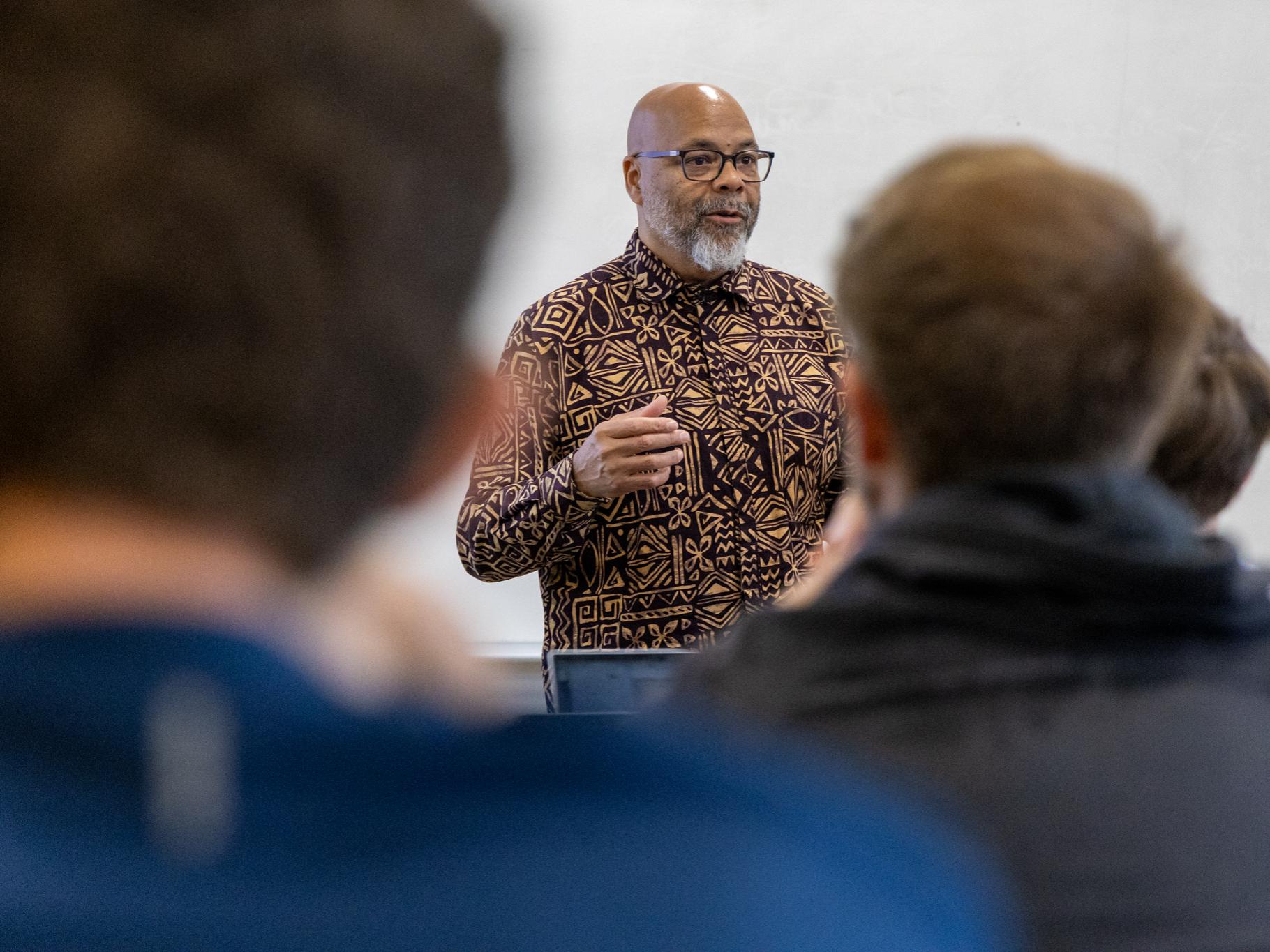 Dr. Bey in a patterned shirt talks to students in blurred foreground focus.