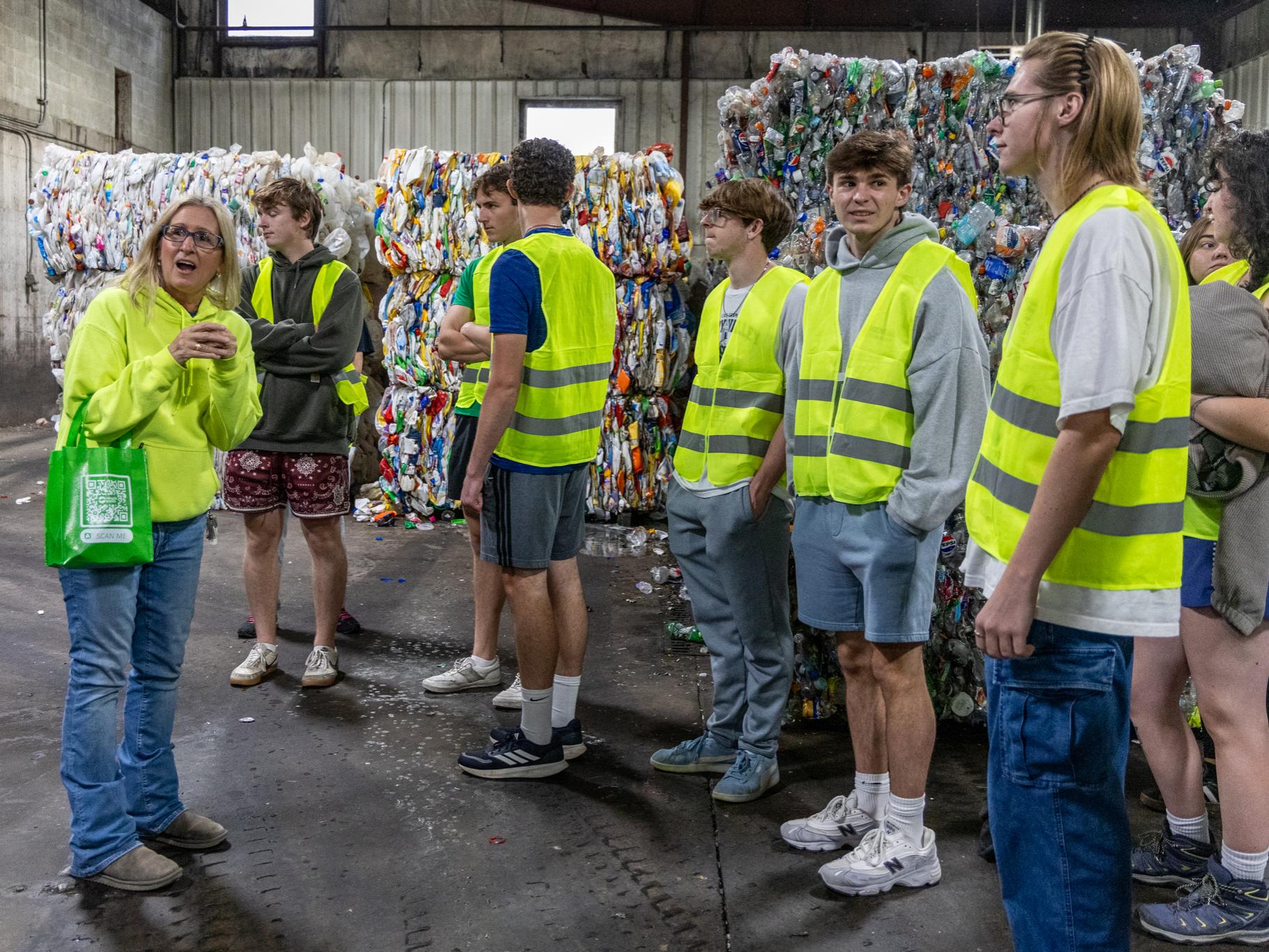 A group of people wearing yellow safety vests are in a recycling facility.