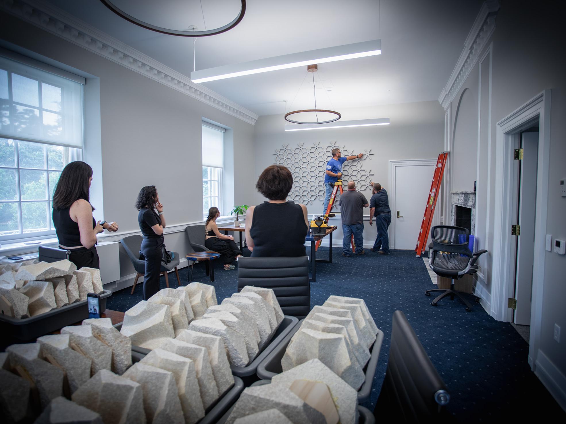 Workers hang the wooden formwork that will hold the mycelium panels of the acoustic wall in an Old Main Office.