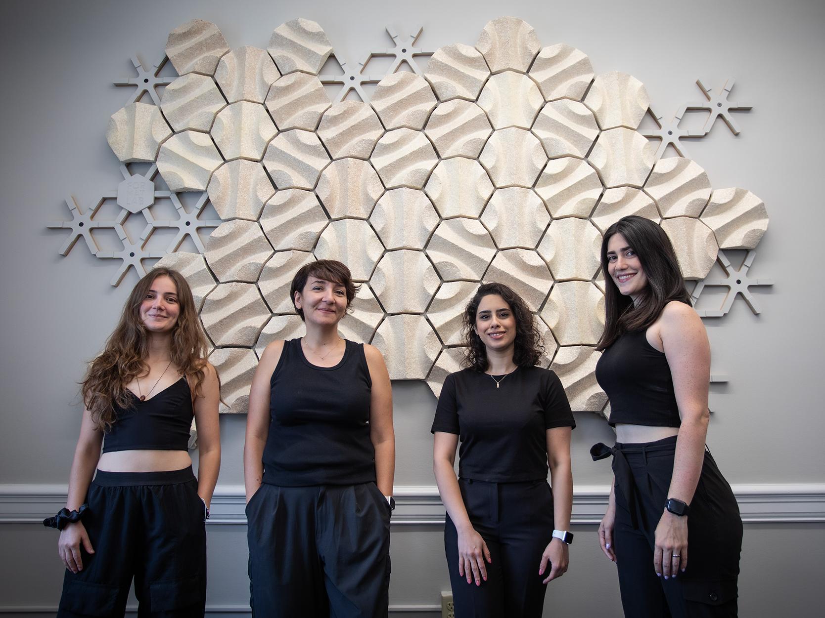 Four individuals in black stand in front of the acoustic wall installed on an office wall in Old Main.