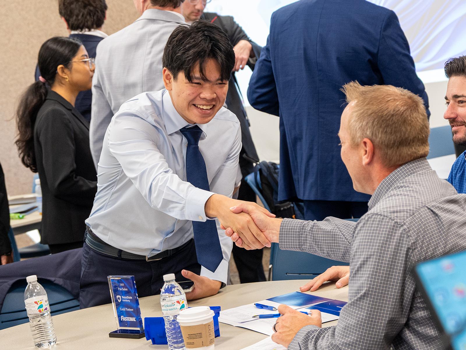 A student shakes the hand of a business representative at a table, during the 2025 Penn State Harrisburg Sales competition