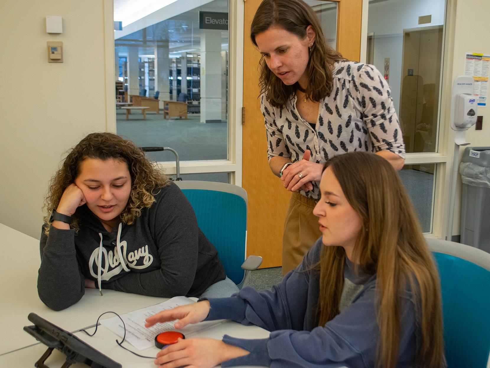 A professor and two students look at an alternative and augmentative communication device that uses a button
