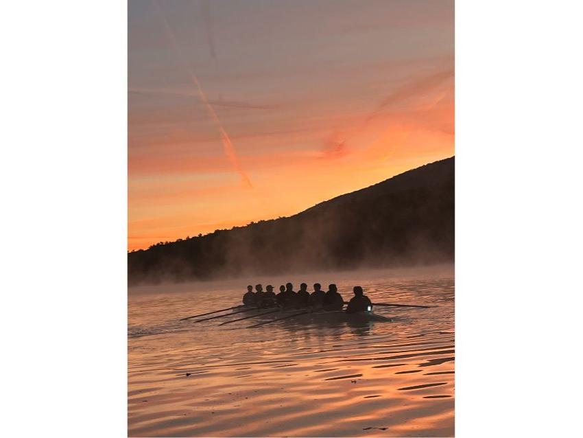 A picture of a rowing team in the shadows on a lake during sunset