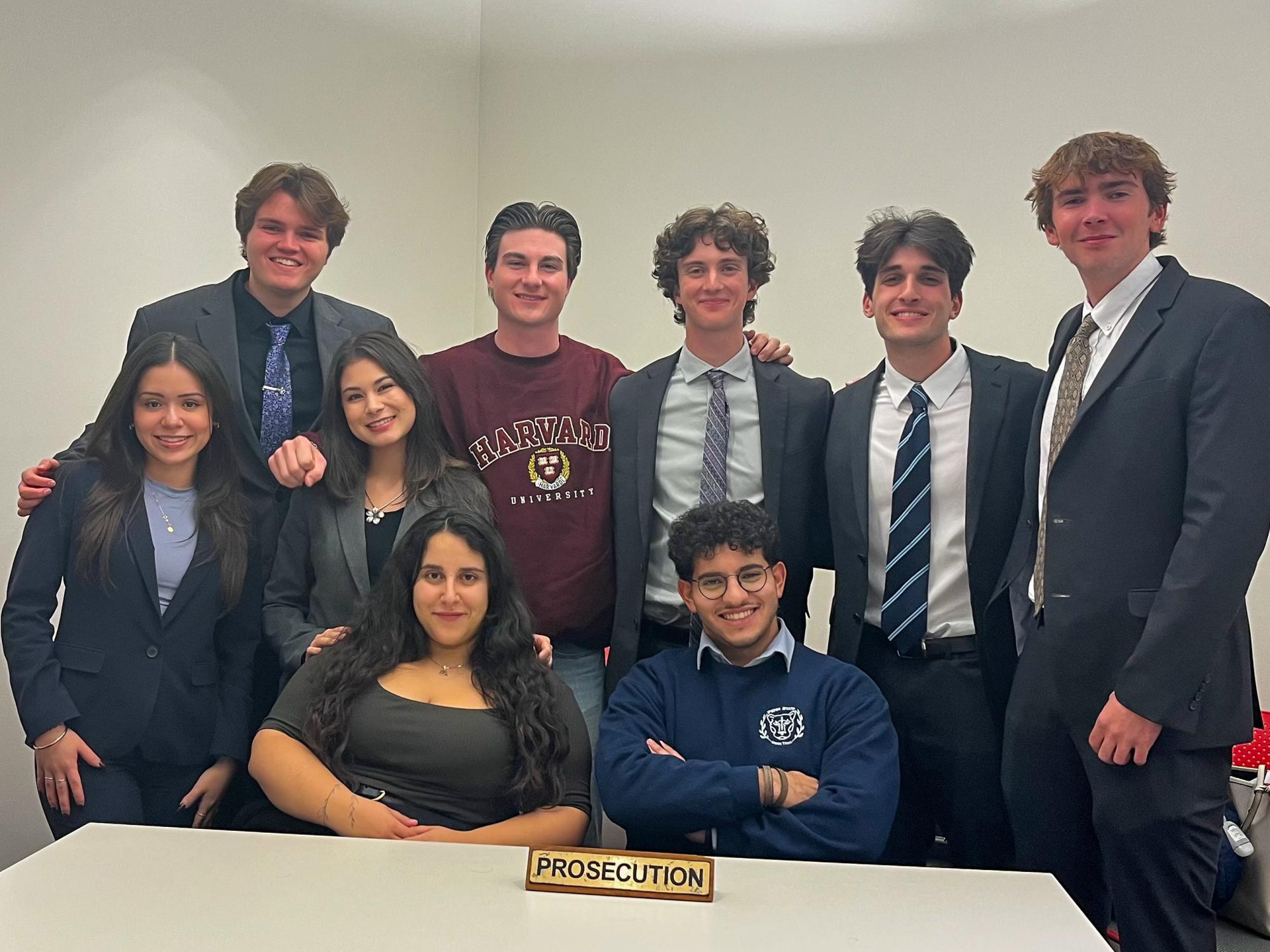 Six people stand and two people are seated in front of a table for the Penn State Mock Trial competition at Harvard University. Oliva Cimbora is standing third from the left.