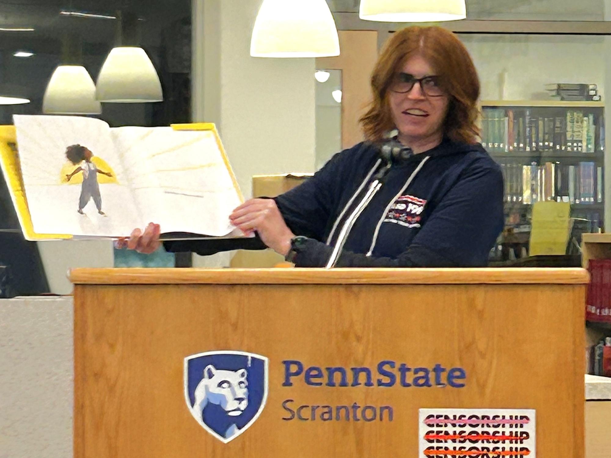 woman holds open book while reading to audience
