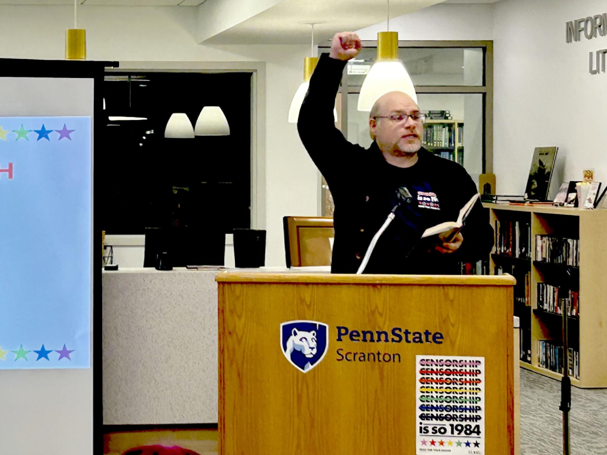 man raised right arm in the air while reading from the podium
