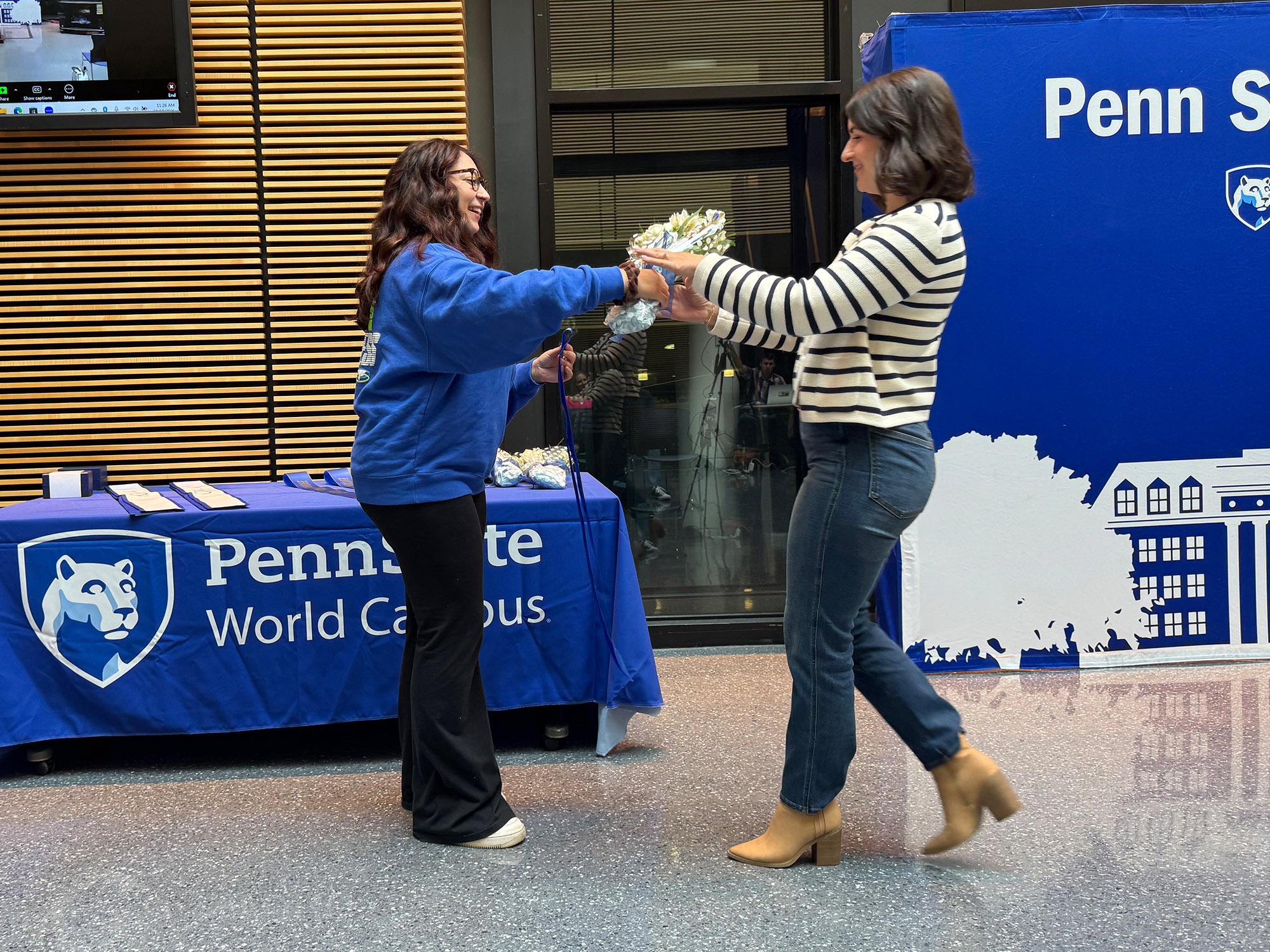 a woman walks over to receive a bouquet from another woman in front of a table