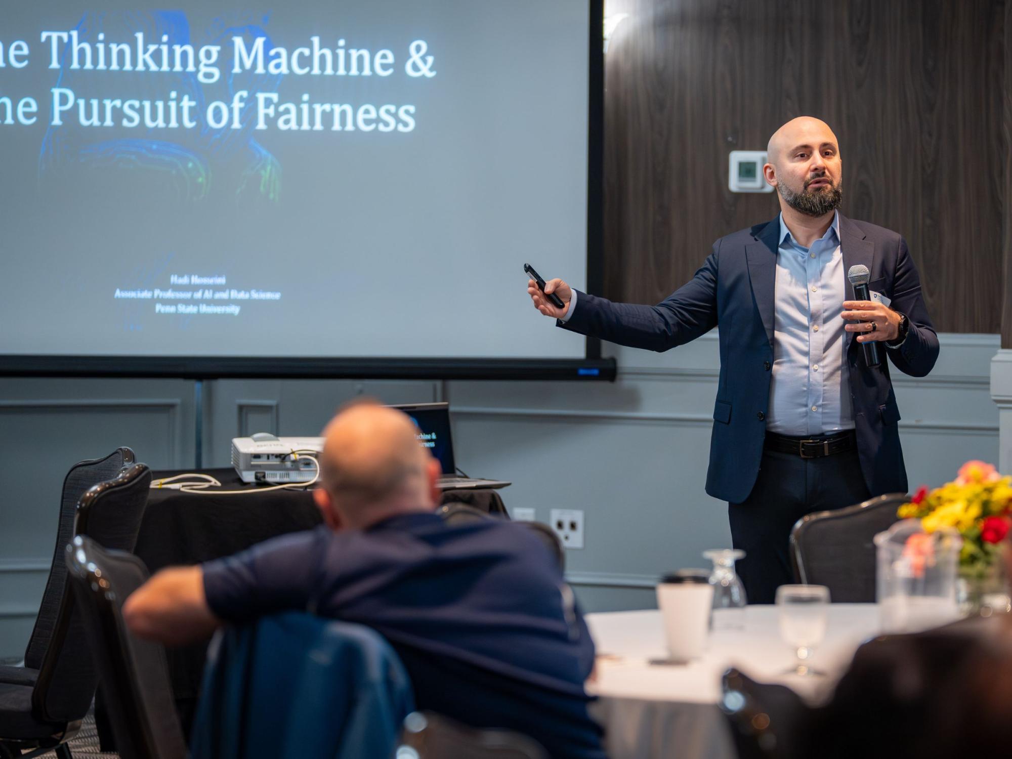 bald person with dark beard presents at a conference