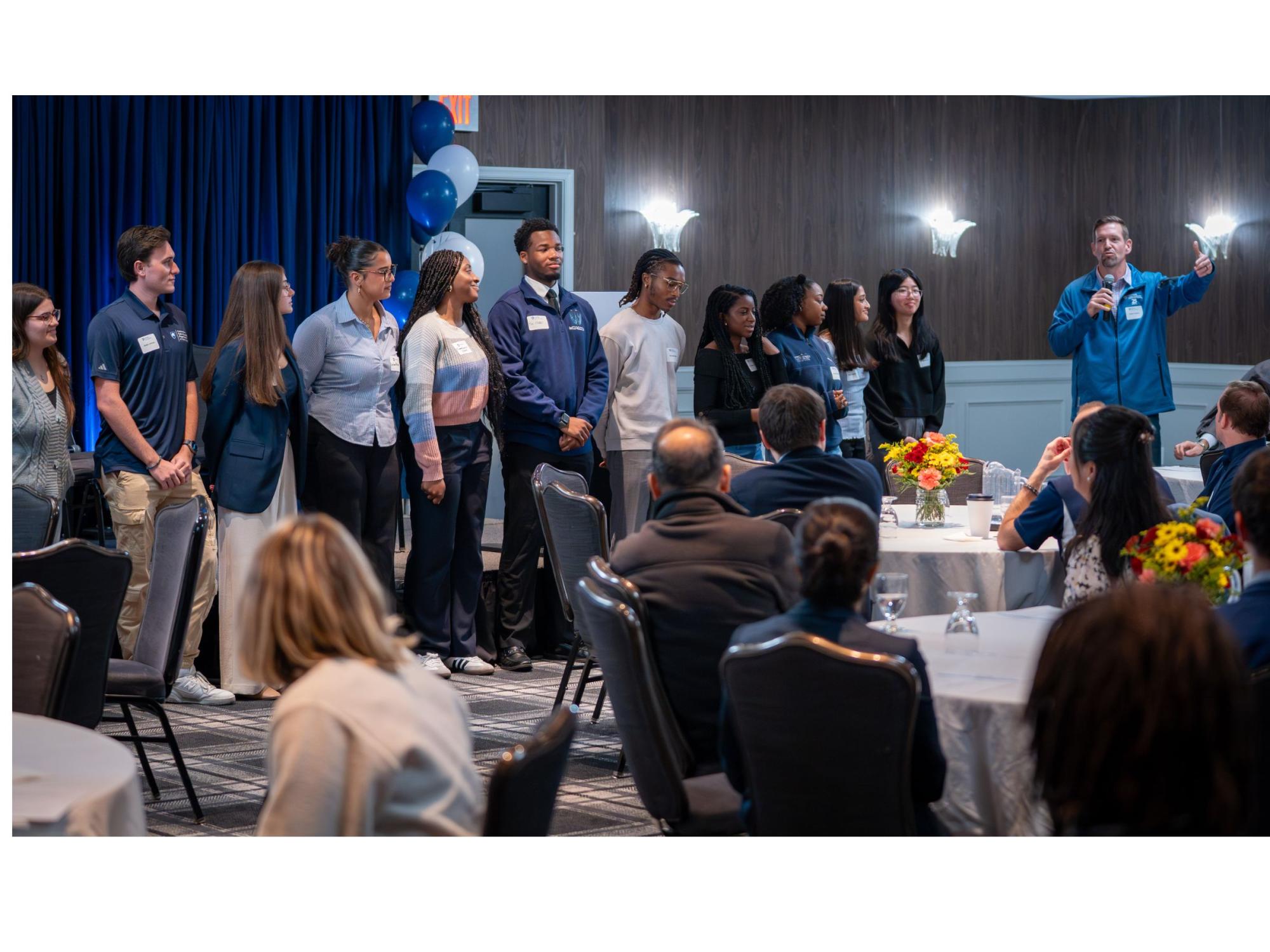 person with microphone introduces row of college students at conference