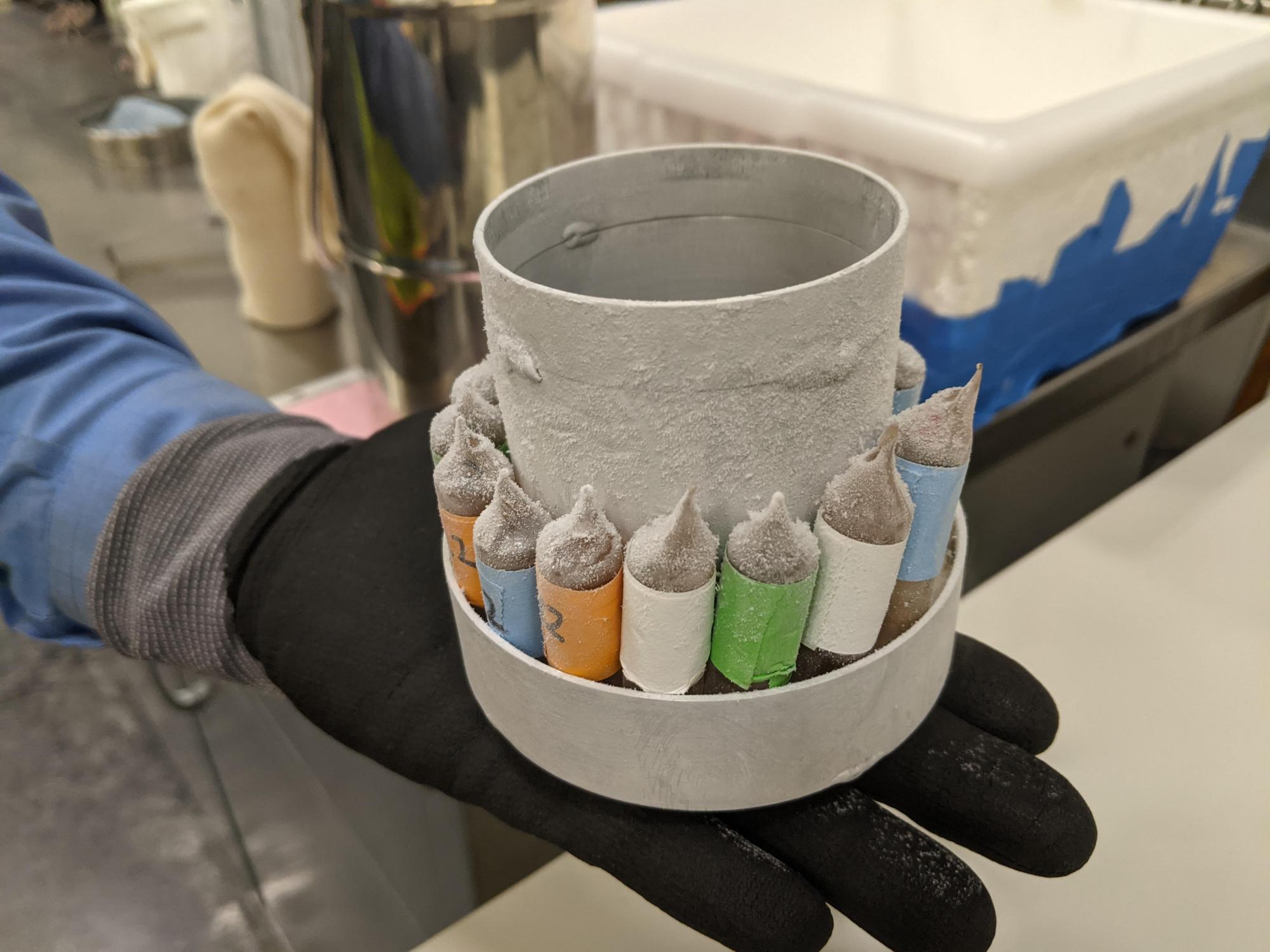 A gloved hand displays frozen test tubes. 