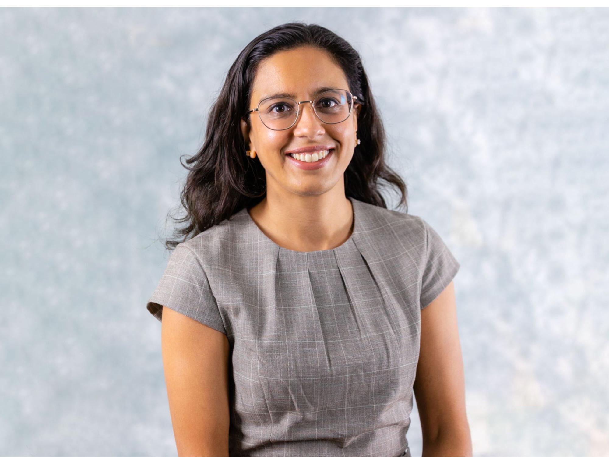 headshot person with long dark hair, glasses, gray attire