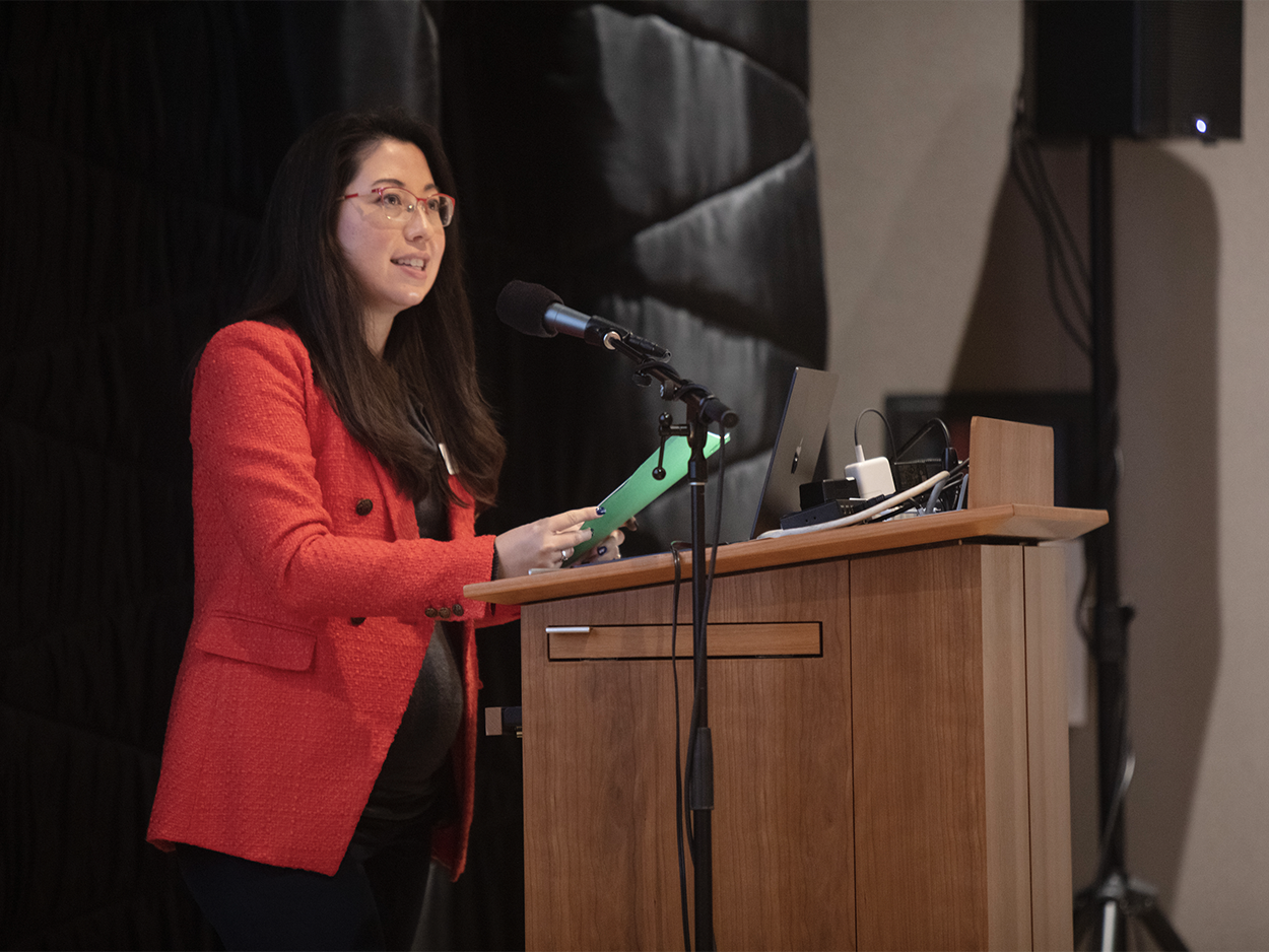 Woman in a red blazer standing and speaknig at a podium