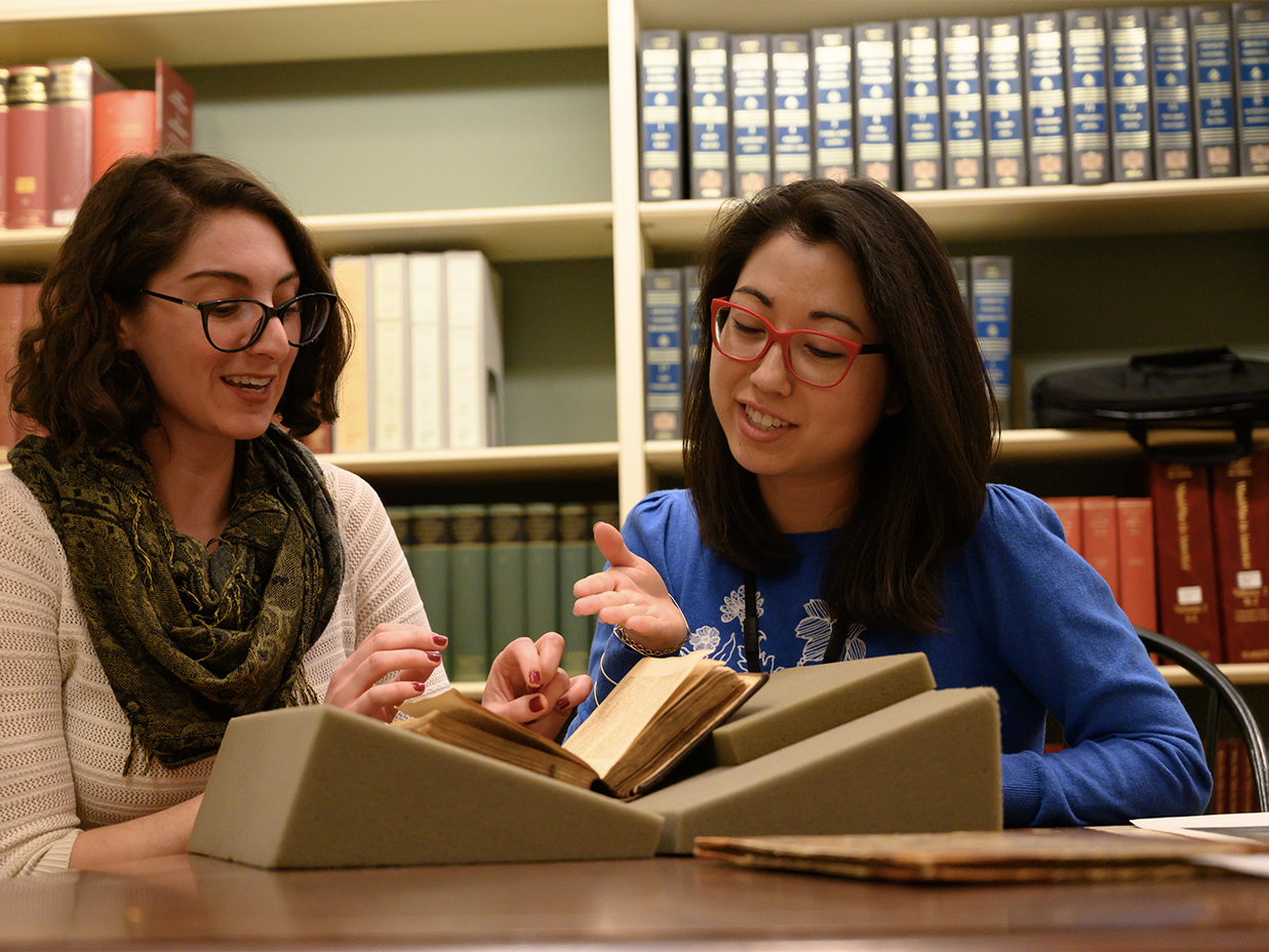 Two women sitting with a book in a library