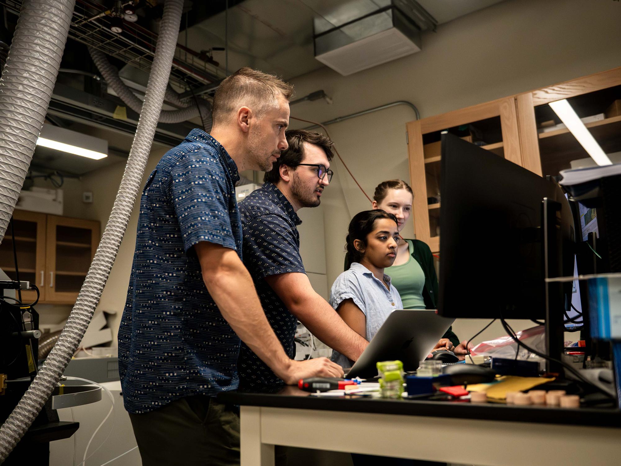 A team of researchers stand at a computer