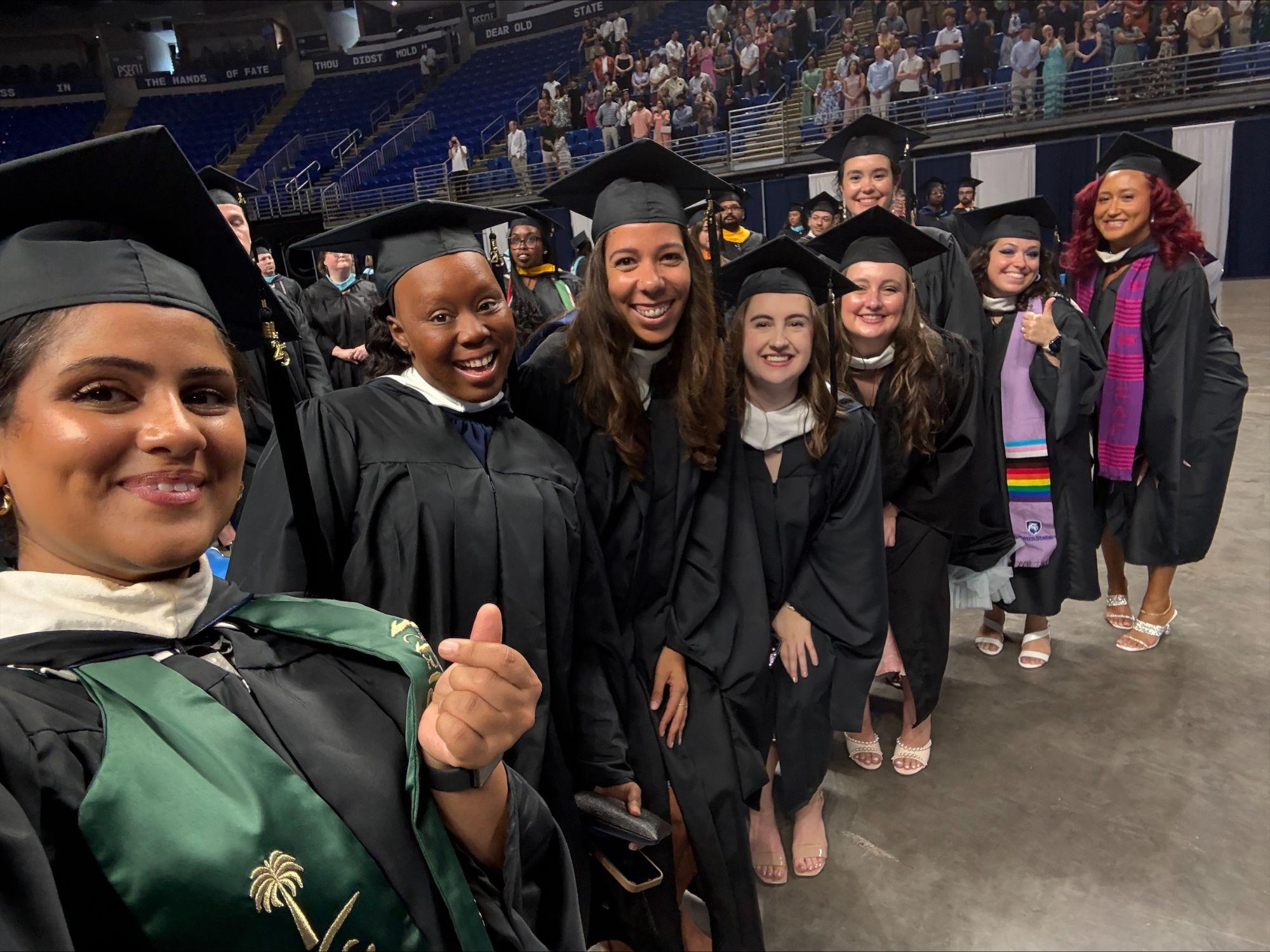 Eight people wearing graduation caps and gowns pose for a photo at commencement