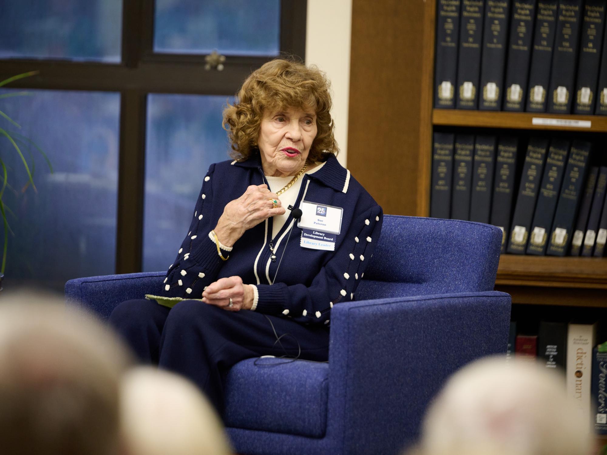 woman pointing to herself as she speaks from a chair