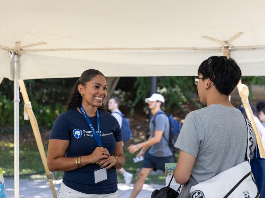 Jasmin Tanner interacts with another student under a tent at the Liberal Arts Undergraduate Festival on Pattee Mall.