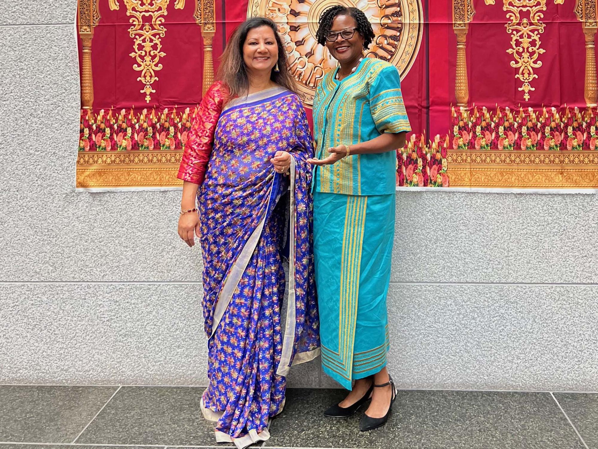 Two women standing next to one another in front of a red banner.