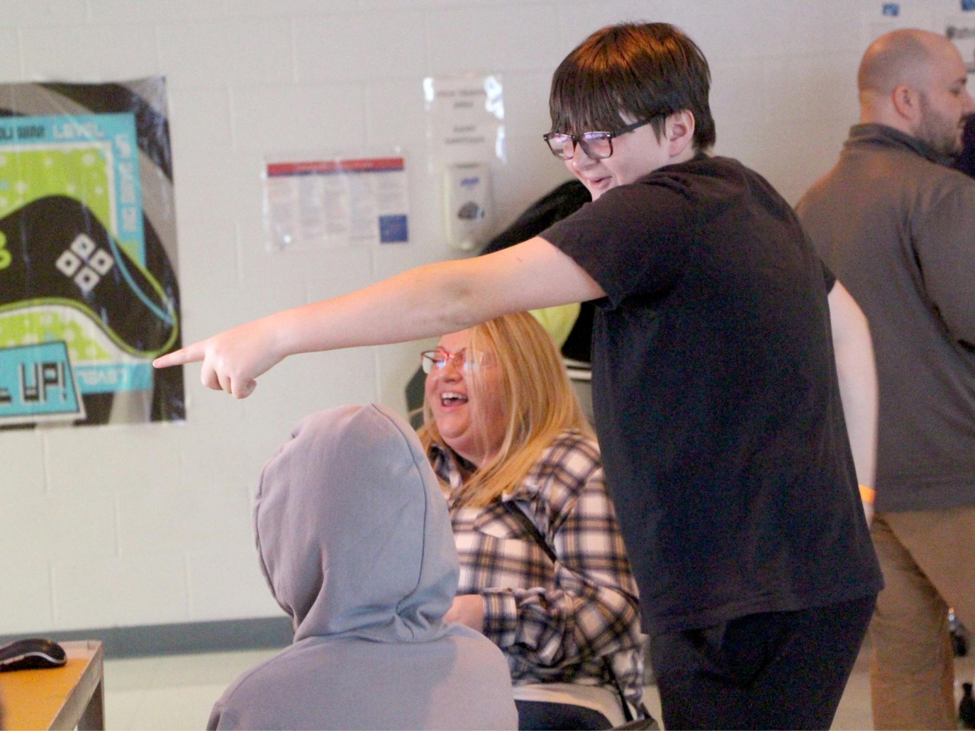 Smiling student points excitedly at a screen while others watch during a classroom gaming activity.